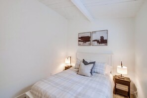 Une chambre à coucher comprenant un lit, deux tables de chevet, deux lampes fixées au mur et deux tableaux encadrés accrochés au mur.