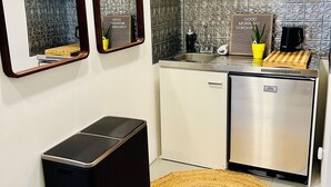 A compact kitchenette with a refrigerator, sink, and a small trash bin.