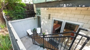 A residential outdoor area with a concrete staircase, a black metal railing, a brick wall, and a small patio with a table and chairs.