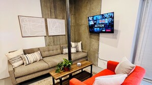 A living room with a grey sofa, a red armchair, a wooden coffee table, and a TV mounted on the wall.