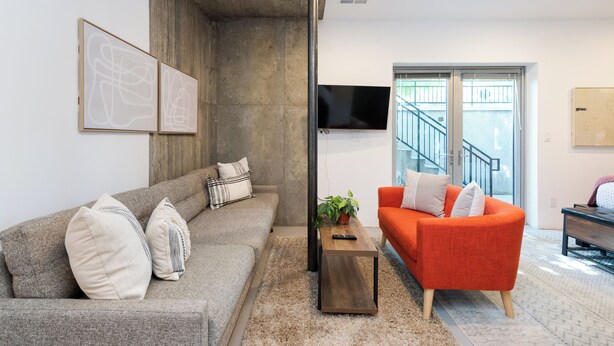A modern living room with a grey sofa, an orange armchair, a coffee table, and a TV mounted on the wall.