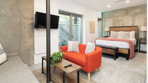 A modern hotel room with a large bed, a sofa, a TV mounted on the wall, and a staircase leading to an outdoor area.