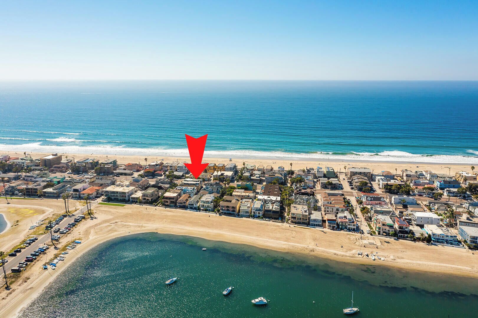 An aerial view of a coastal town with a beach, marina, and residential buildings.