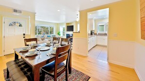 Un coin repas avec une table en bois dressée pour quatre personnes, un canapé et une cuisine en arrière-plan.