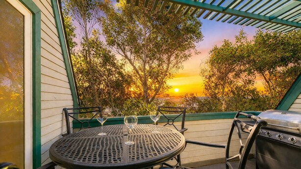 Une terrasse avec une table ronde et des chaises, un barbecue et une vue sur le coucher de soleil.