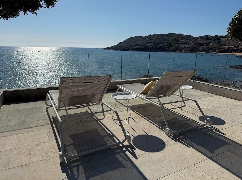 Une terrasse avec deux chaises longues donnant sur une étendue d’eau et un paysage vallonné.