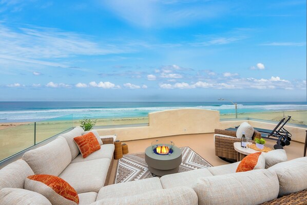 A balcony with a sofa, a fire pit, and a view of the beach.