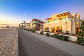 A beachfront hotel with a modern design, featuring a poolside area with sun loungers and a covered seating area.