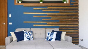 A grey sectional sofa with two blue and white patterned pillows, a wooden slat wall, and a small shelf with two potted plants. - Brisa Azul | Poolfront | Walk to Beach | Wi-Fi (Las Terrenas)