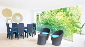 A modern outdoor dining area with wicker furniture, a glass balustrade, and a view of lush greenery. - Brisa Azul | Poolfront | Walk to Beach | Wi-Fi (Las Terrenas)