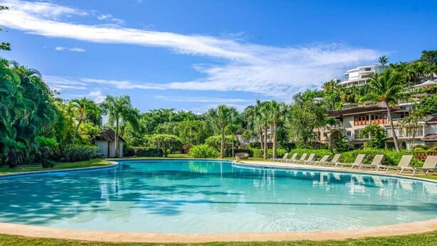 A swimming pool with lounge chairs, surrounded by lush greenery and a clear blue sky. - Brisa Azul | Poolfront | Walk to Beach | Wi-Fi (Las Terrenas)