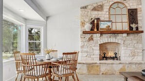 Comedor con chimenea de piedra, sillas de madera y una mesa dispuesta para cuatro.