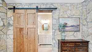 Un interior rústico con puerta corredera de madera, paredes de piedra, un espejo y un aparador.