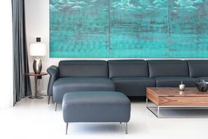 A modern living room with a sectional sofa, a round coffee table, and a large abstract painting on the wall. - Luxury Villa Black Cube with heating pool (Brašina)
