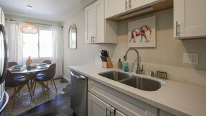 Una cocina moderna con armarios blancos, un lavamanos doble y una zona de comedor con una mesa y sillas.