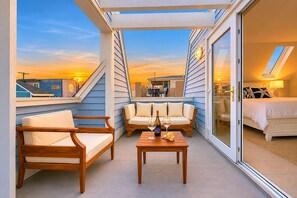En balkon med sofa, stole og et bord med vinglas og en vinflaske.