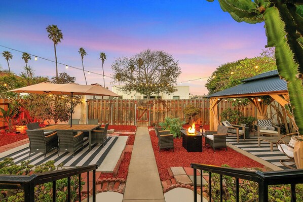 An outdoor patio area with a fire pit, seating, and a wooden fence. - Walk to Beach W/Parking, Outdoor BBQ & Fire Pit! (San Diego)