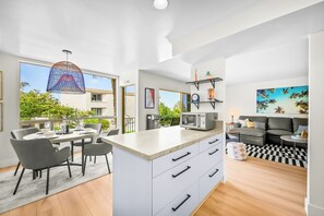 A modern kitchen with a dining area, a living room with a sofa and coffee table, and a large window with a view of trees. - Pet Friendly 2 bedroom in Point Loma Overlooking Kellogg Beach - Stay for 30 days! (San Diego)