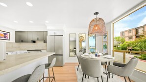 A modern kitchen with a central island, a dining area with a round table and chairs, and large windows offering a view of the outside. - Pet Friendly 2 bedroom in Point Loma Overlooking Kellogg Beach - Stay for 30 days! (San Diego)