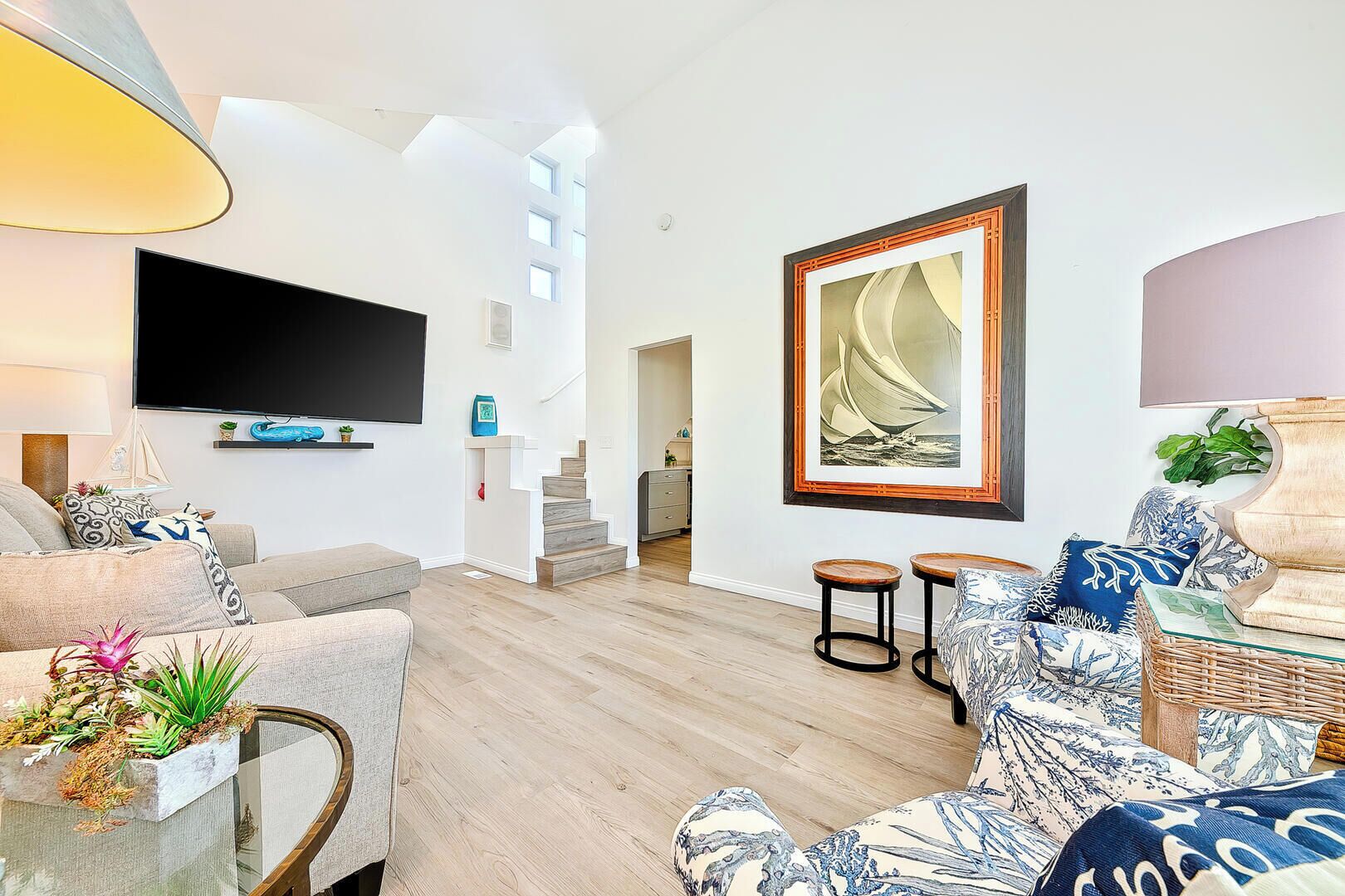 Ein modernes Wohnzimmer mit Flachbildfernseher, einer Treppe und einem großen Gemälde eines Segelboots.