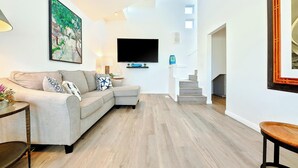 Una sala de estar con un sofá, un televisor de pantalla plana, una escalera y un cuadro en la pared.