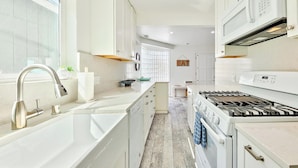 Una cocina moderna con muebles blancos, un grifo de acero inoxidable, horno empotrado y microondas.