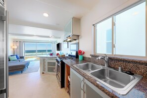 A modern kitchen with granite countertops, stainless steel appliances, and a large window overlooking the beach. - Great Reviews, Beachfront, Endless Sunset Views! (San Diego)
