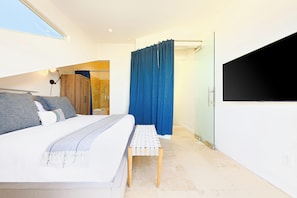 A modern bedroom with a large bed, a small bench, a wardrobe, and a shower area. - Great Reviews, Beachfront, Endless Sunset Views! (San Diego)