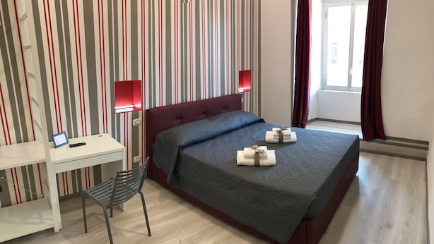 Et hotelværelse med seng, skrivebord, stol og to sengeborde med lamper.