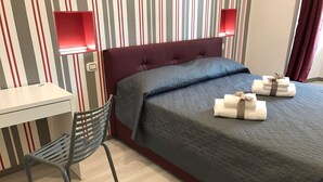 A hotel room with a bed, a desk, a chair, and two wall-mounted lamps. - Superior room 1 3 people Piazza Bologna (Roma)