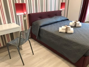 A hotel room with a bed, a desk, a chair, and two wall-mounted lamps. - Superior room 1 3 people Piazza Bologna (Roma)