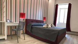 A hotel room with a bed, a desk, and a chair. There is a window with curtains.