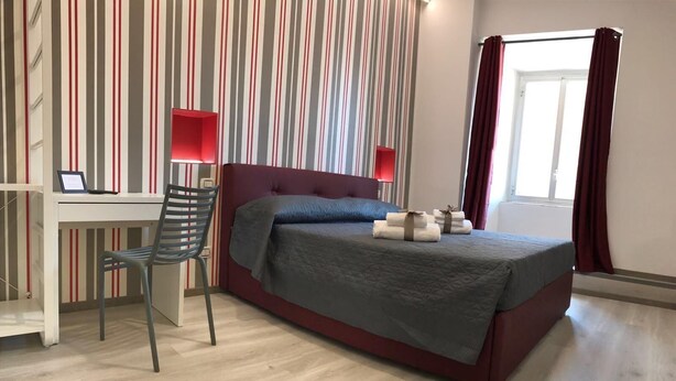 A hotel room with a bed, a desk, and a chair. There is a window with curtains. - Superior room 1 3 people Piazza Bologna (Roma)