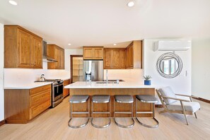 Eine moderne Küche mit Holzausbau, einem Edelstahlkühlschrank, einem eingebauten Ofen und einer Bar mit Sitzgelegenheiten.