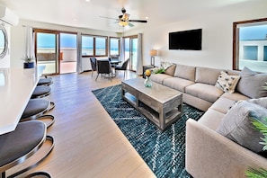 Ein modernes Wohnzimmer mit Sofa, Couchtisch und Essbereich, großen Fenstern mit Blick und einem Deckenventilator.