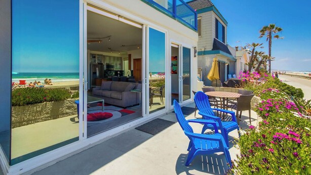 Een accommodatie aan het strand met een balkon, een eethoek met blauwe stoelen en uitzicht op het strand.