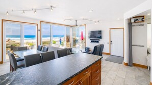 Een moderne keuken met een groot eiland, een eetgedeelte met uitzicht op het strand, en een aan de muur bevestigde televisie.