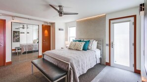 Een moderne slaapkamer met een bed, een bankje, een plafondventilator en een schuifdeur.
