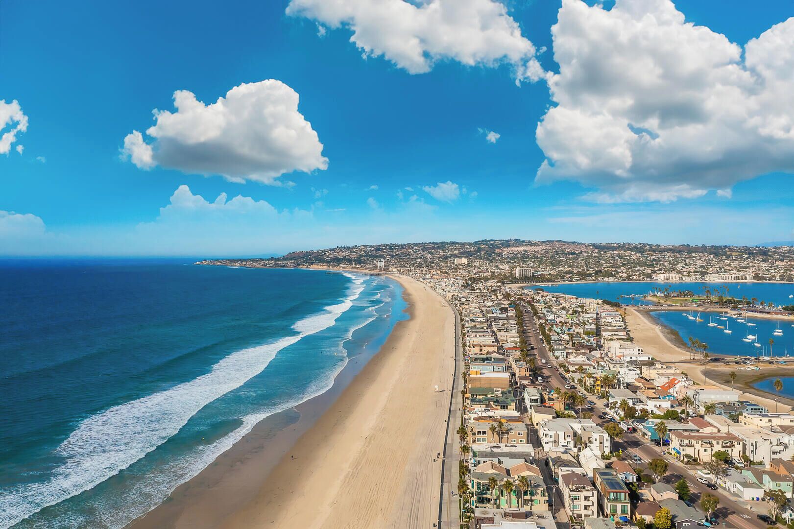 A coastal cityscape with a wide beach, residential buildings, and a marina.