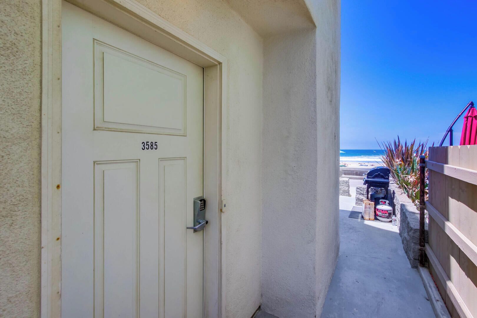 A white door with the number 3585, leading to a balcony with a view of the beach and ocean.
