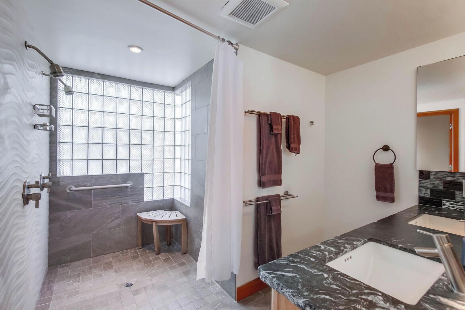 A modern bathroom with a shower, a vanity with a sink, and a window with a view.