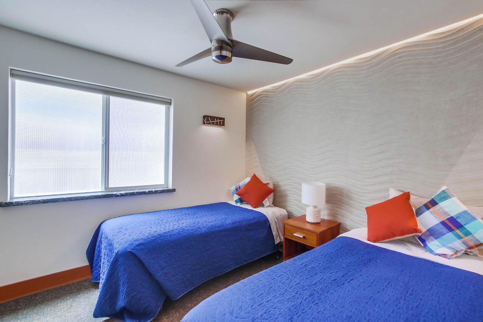 Une chambre d’hôtel avec deux lits, un ventilateur de plafond, une table de chevet et une fenêtre avec des stores.