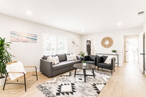Ein modernes Wohnzimmer mit einem grauen Ecksofa, einem runden Couchtisch und einem schwarzen Ledersessel.