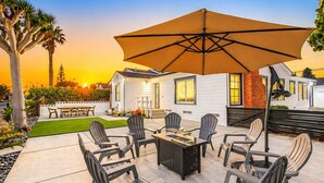 Een buitenterras met een tafel, stoelen, een grote parasol en een huis op de achtergrond.