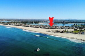 Luftaufnahme einer Küstenstadt mit Strand, einer Marina und einem großen roten Pfeil, der auf einen bestimmten Bereich zeigt.