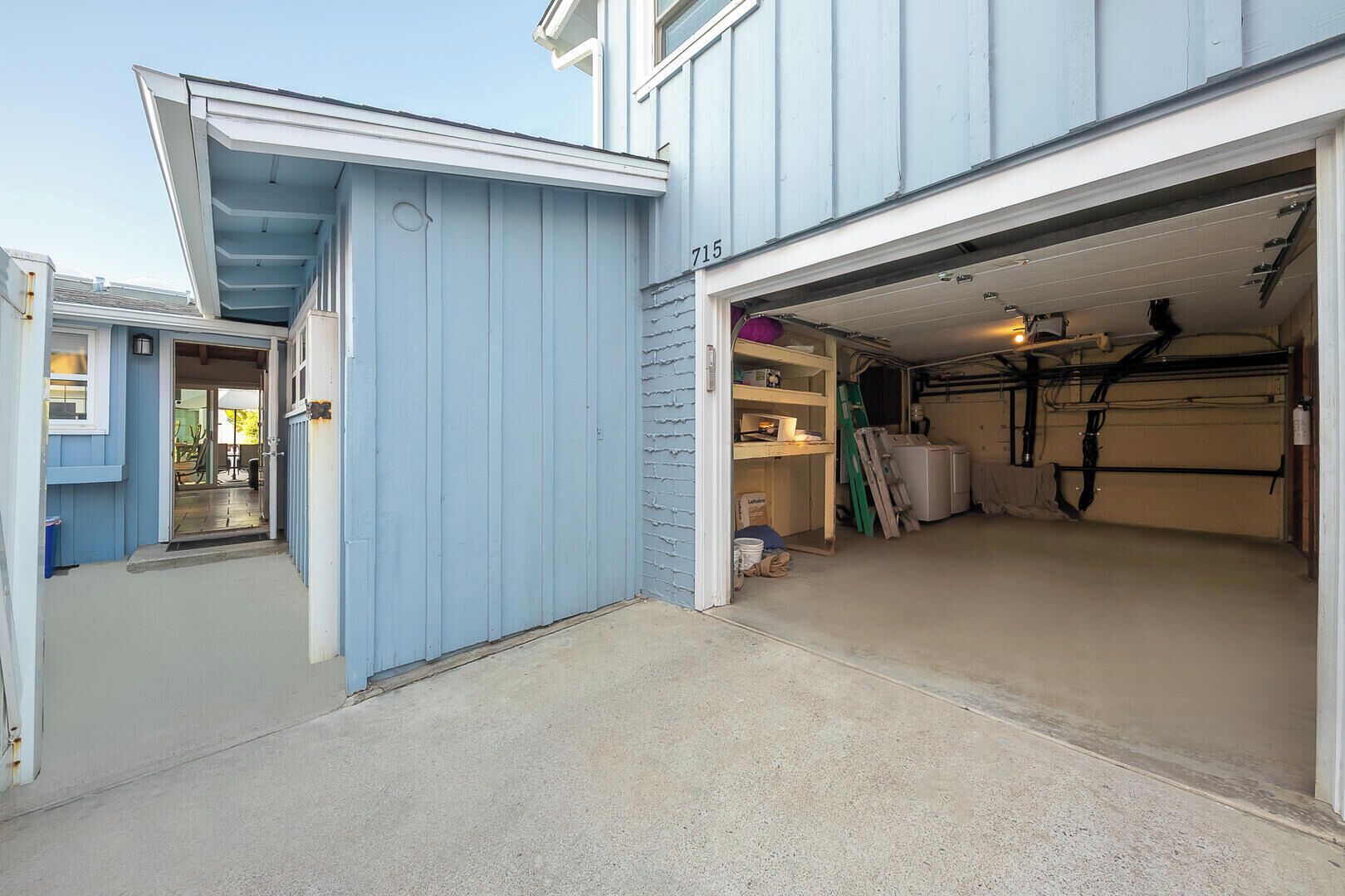 A garage with a concrete floor, a white garage door, and various items like a ladder and a washing machine.