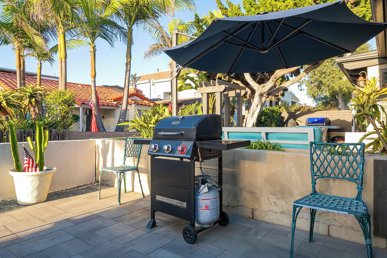 An outdoor patio with a grill, two chairs, and a potted plant with an American flag.