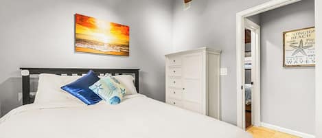 Un dormitorio con cama, ventilador de techo, un cuadro, armario y un cartel en la pared.