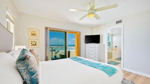 Un dormitorio con cama, televisor, ventilador de techo y vista a la playa.