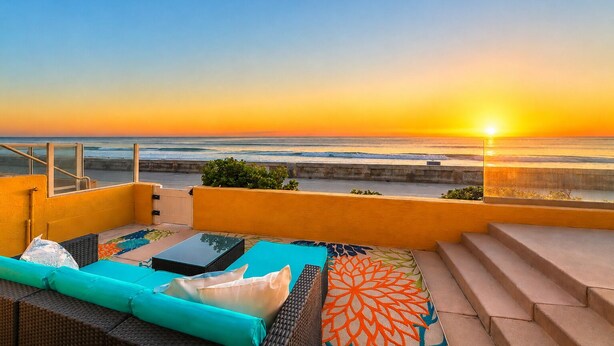 Una terraza con vista al océano al atardecer, mobiliario exterior y una escalera que baja.